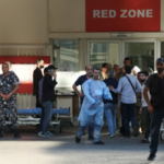 A group of people, including medical staff and other individuals, standing outside an emergency hospital entrance marked "Red Zone."